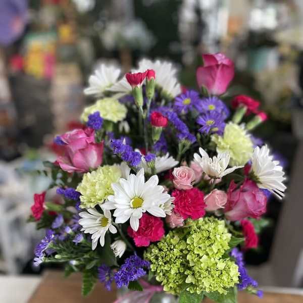 Mixed bouquet of pink roses, white daisies, and purple flowers in a glass vase