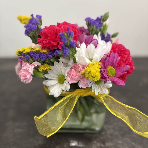 Colorful bouquet in a square glass vase with a yellow ribbon