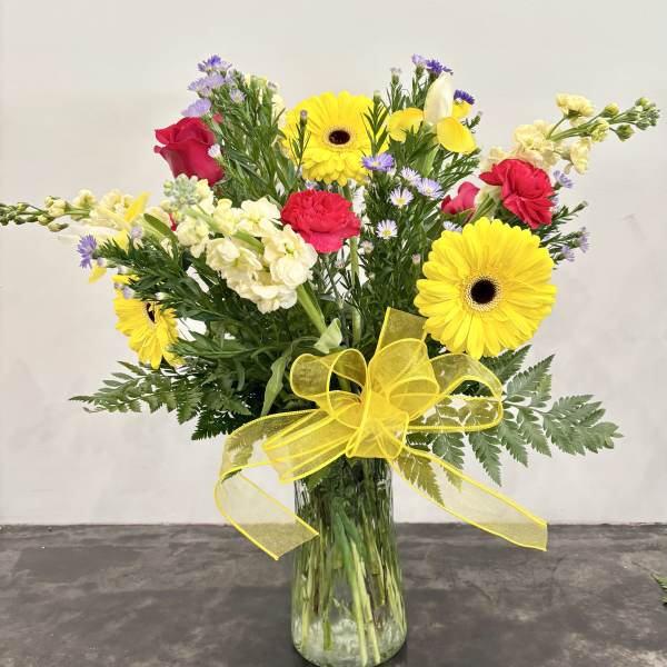 Bouquet of yellow gerbera daisies, red roses, and white snapdragons in a glass vase
