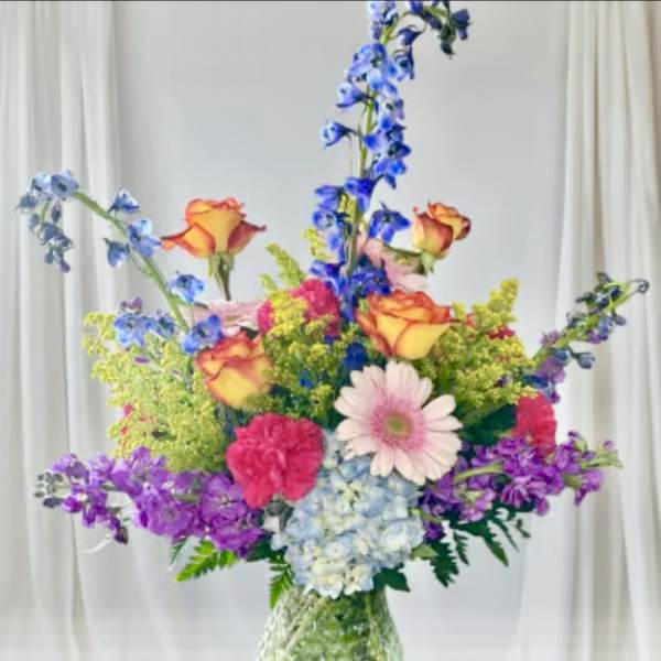 Colorful mixed bouquet with roses, gerbera daisy, hydrangea, and tall blue flowers in a vase