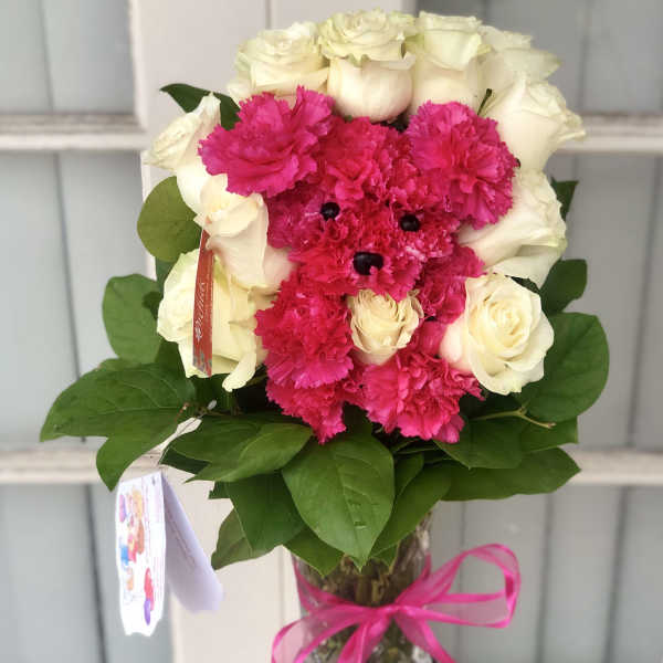 Pink carnations and white roses arranged in a glass vase with a ribbon