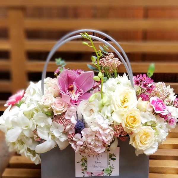 Low box arrangement of white hydrangeas, cream roses, and pink orchids in a gray handled container