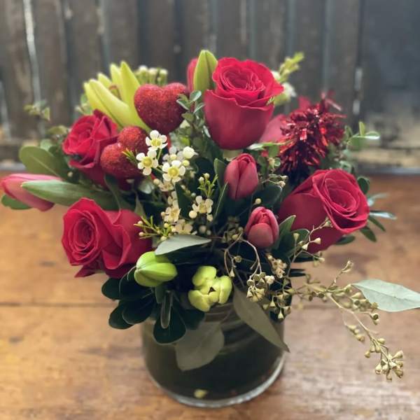 Red roses and tulips arranged in a glass vase with small white filler flowers