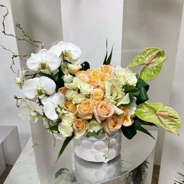 White orchids and peach roses arranged in a white vase