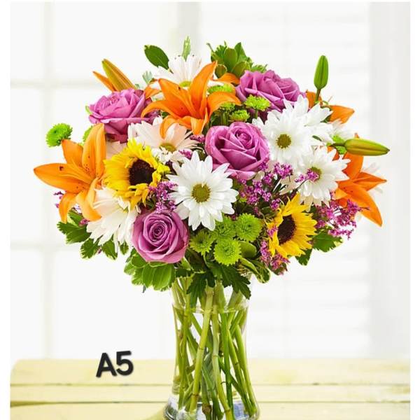 Mixed bouquet of orange lilies, purple roses, sunflowers, and white daisies in a glass vase