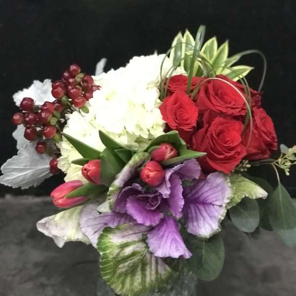 Bouquet of red roses, white hydrangea, and purple flowers in a glass vase