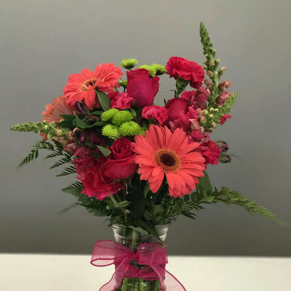 Pink and coral mixed flowers in a glass vase with a pink ribbon