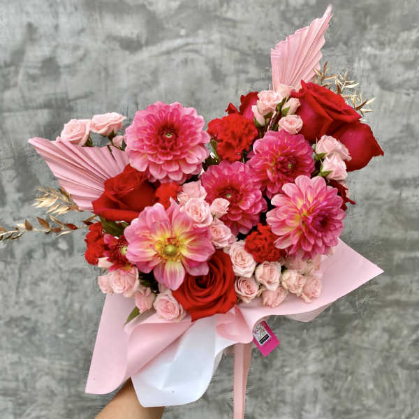 Pink and red bouquet with roses and dahlias wrapped in pastel paper