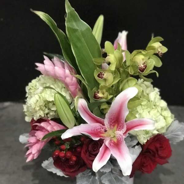 Bouquet of pink lilies, green orchids, and red roses in a white vase