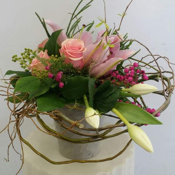 Pink roses and lilies in a glass vase with curly branches