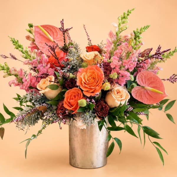 Mixed bouquet of orange and pink flowers in a silver vase