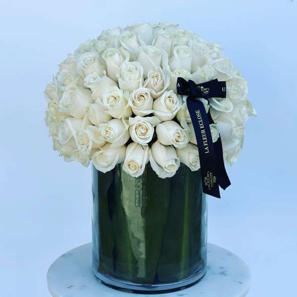 White rose bouquet in a tall glass vase with a black ribbon