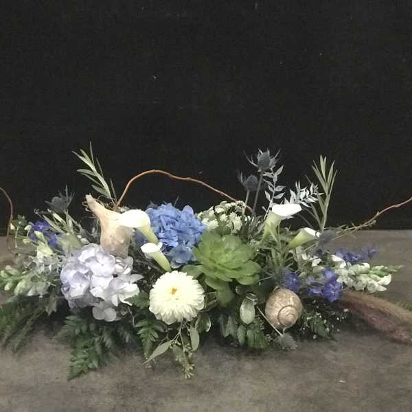 Low floral arrangement with blue hydrangeas, white calla lilies, and succulents