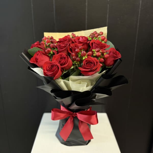 Bouquet of red roses with berry accents wrapped in black paper and a red ribbon