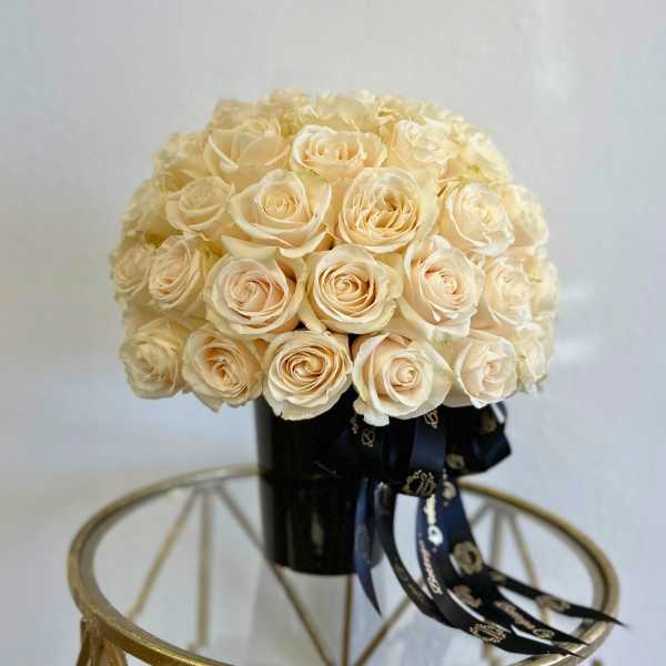 Cream rose bouquet in a black vase with dark ribbon