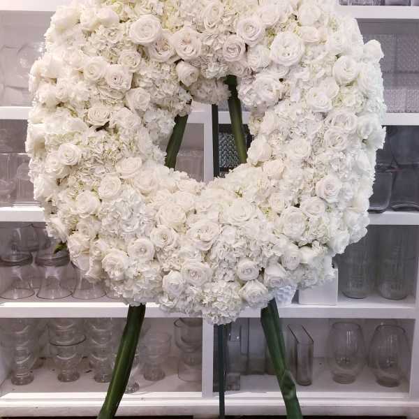 Large white floral wreath on a stand with roses and hydrangeas