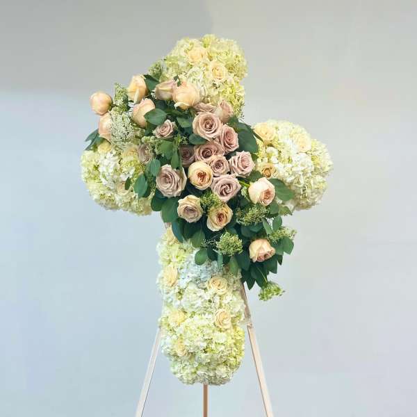 Large floral cross on an easel with cream roses and pale hydrangeas