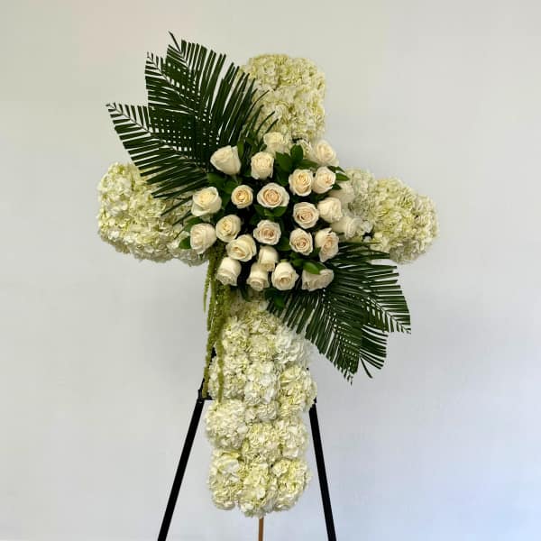 White floral cross arrangement with roses and hydrangeas on a stand
