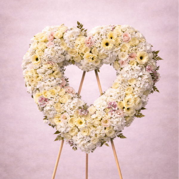 Large heart-shaped standing wreath of white and pale pink flowers on a wooden easel.