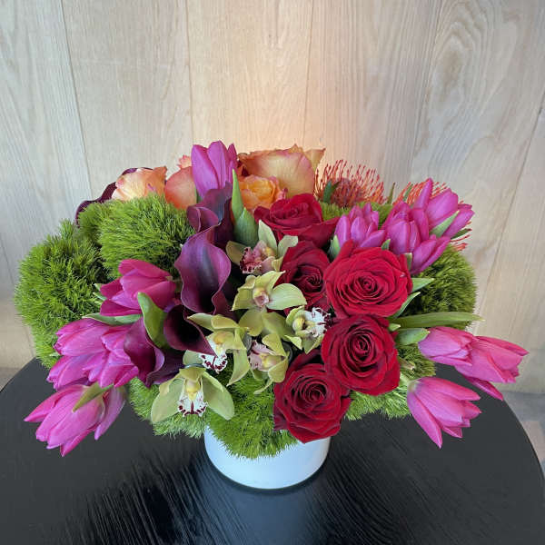 Pink tulips, red roses, and orchids arranged in a white vase