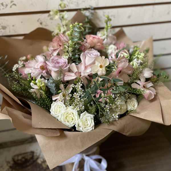 Bouquet of blush and white roses with pale pink flowers in brown paper