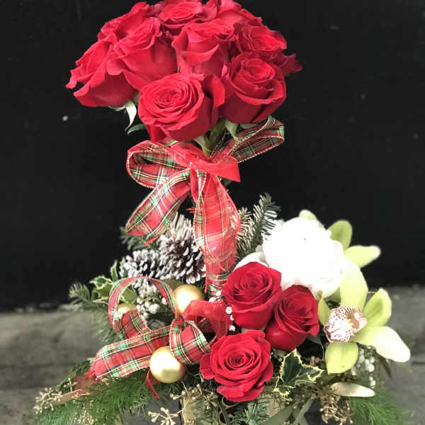 Red roses arranged in a festive holiday centerpiece with ribbon and ornaments
