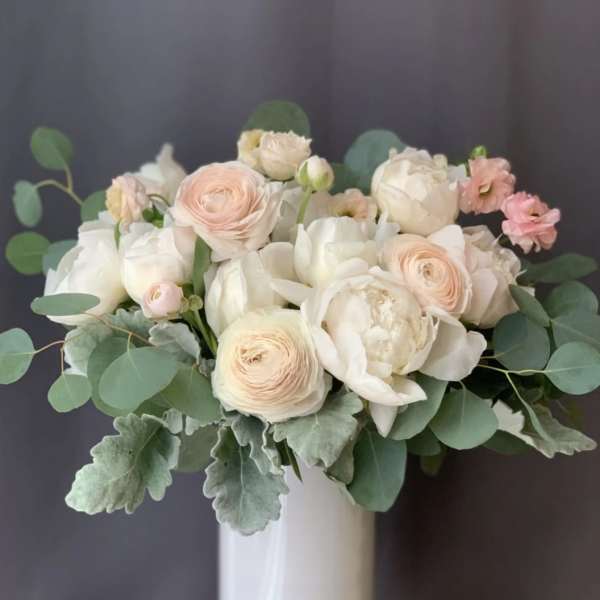Blush and white bouquet in a white vase with round green foliage