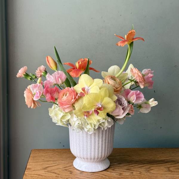 Pastel floral arrangement in a white vase with orchids, roses, and ranunculus