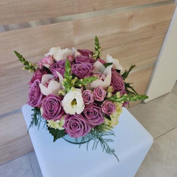 Low round arrangement of lavender roses with white blooms in a clear glass bowl vase