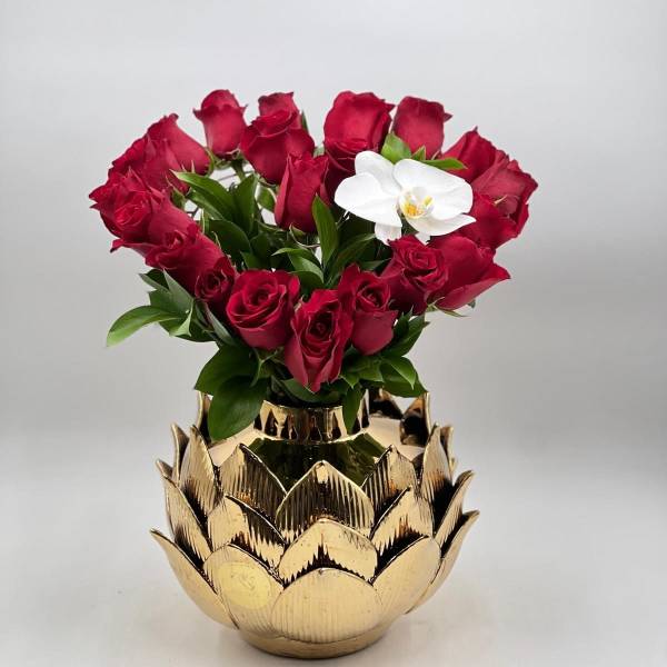 Red roses arranged in a gold lotus-shaped vase with one white orchid bloom