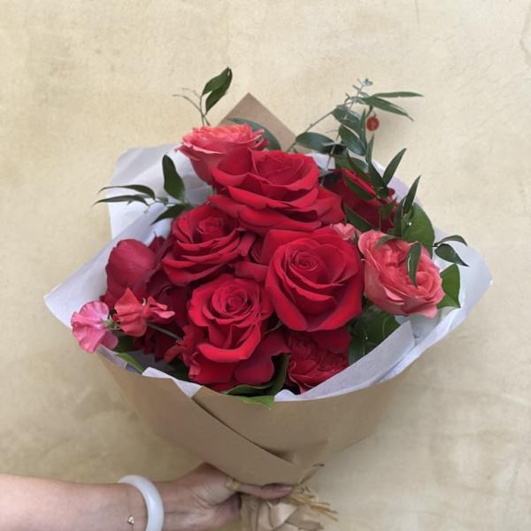 Handheld bouquet of red and pink roses wrapped in brown paper