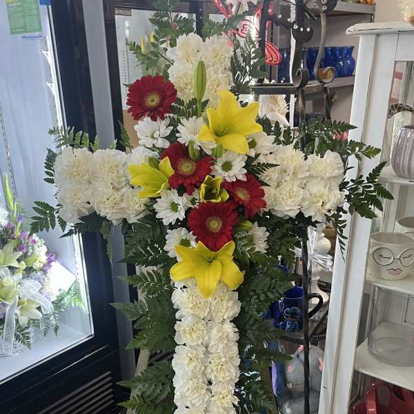 Standing floral cross with white carnations, red gerberas, and yellow lilies