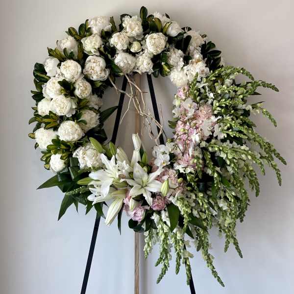 Large floral wreath with white blooms, lilies, and pink accents on a stand