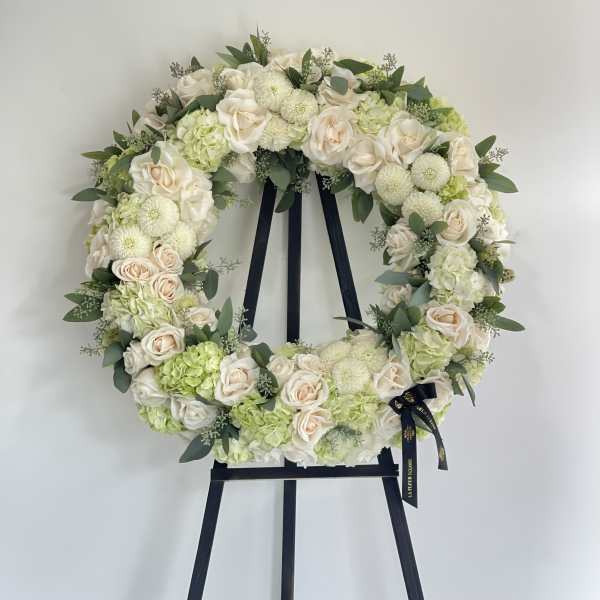 Round floral wreath of cream roses and pale green blooms on a black easel