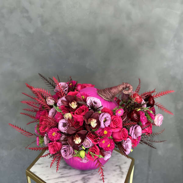 Pink and burgundy floral arrangement in a round vase with a wrapped handle