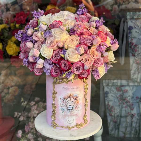 Pink and lavender roses arranged in a tall pink box with a lion illustration