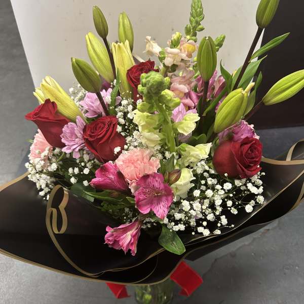 Bouquet of red roses, lilies, and pink flowers wrapped in black paper