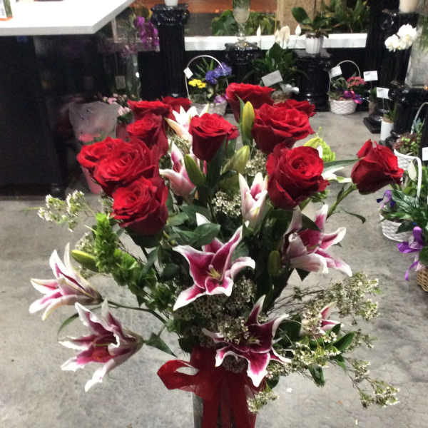 Red roses and pink lilies in a clear glass vase with a red ribbon