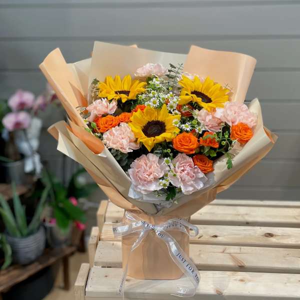 Bouquet of sunflowers, orange roses, and pale pink carnations wrapped in tan paper