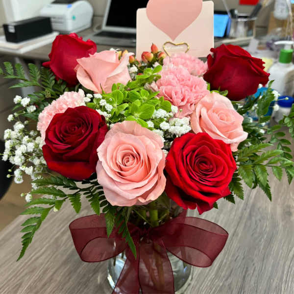 Bouquet of red and pink roses in a glass vase with a burgundy ribbon