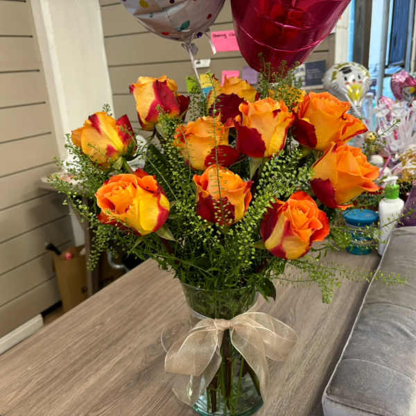 Bouquet of orange and red roses in a glass vase with a ribbon