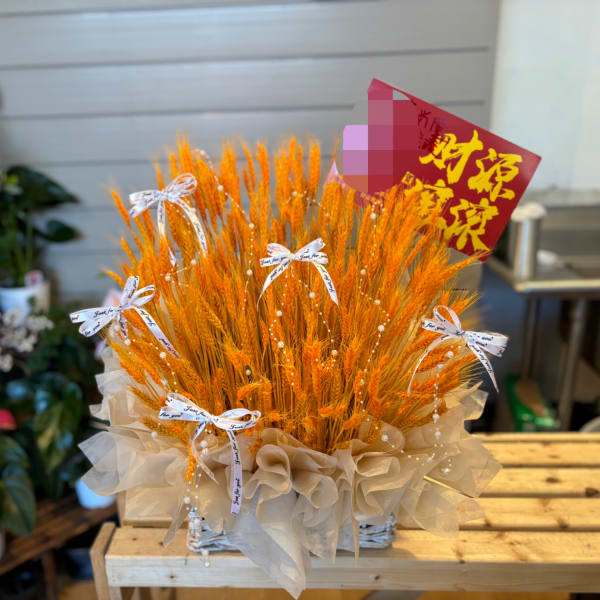 Orange wheat arrangement in a basket with white ribbon bows and a red sign