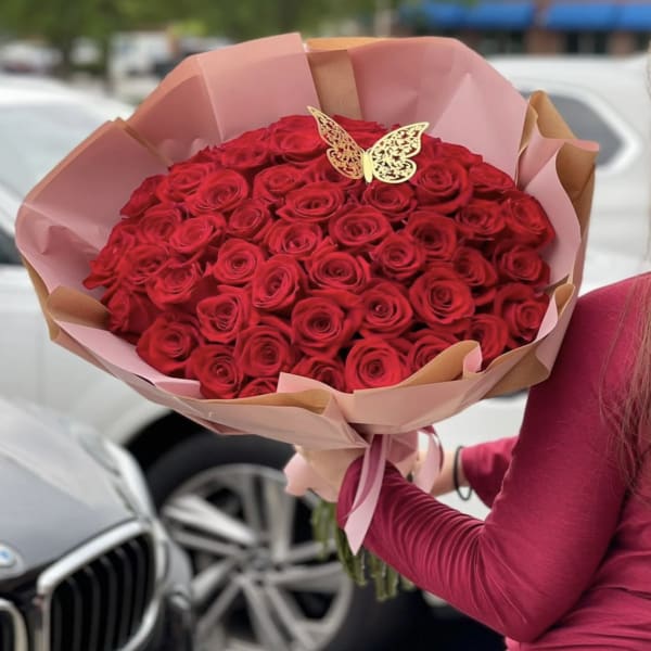Large bouquet of red roses wrapped in pink paper with a butterfly topper