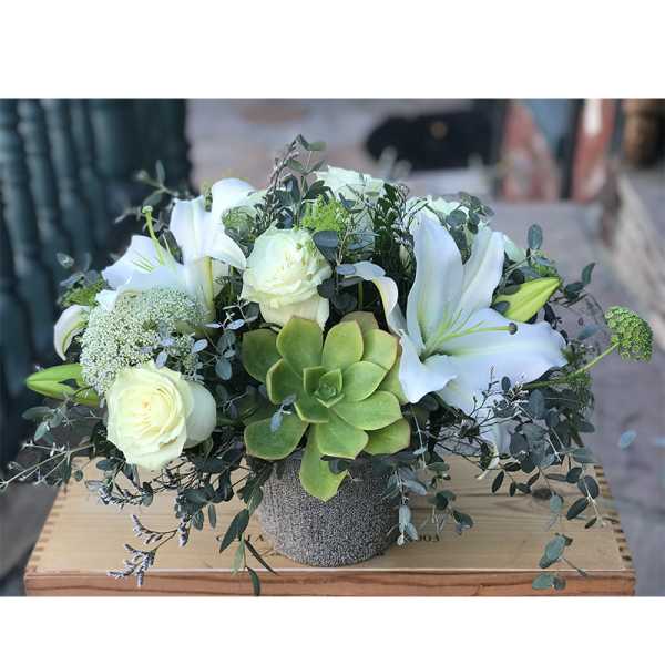 White lilies and roses arranged with a green succulent in a textured pot