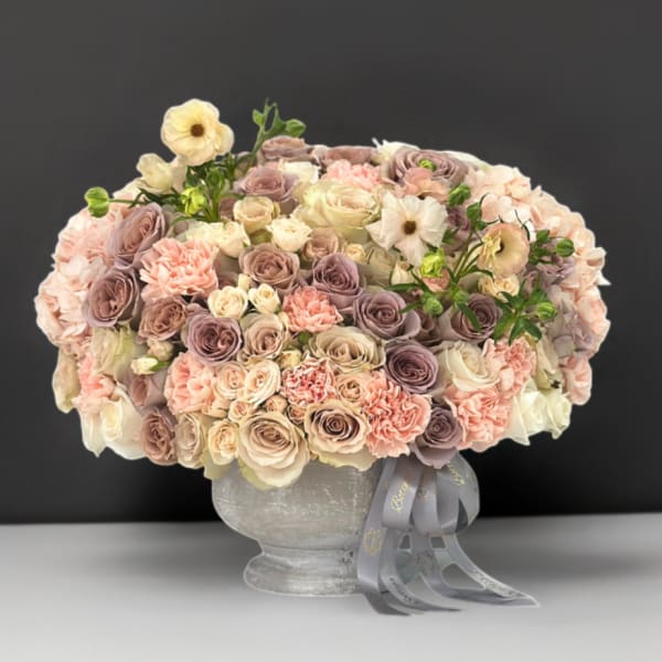 Large pastel bouquet of roses and carnations in a gray vase with ribbon
