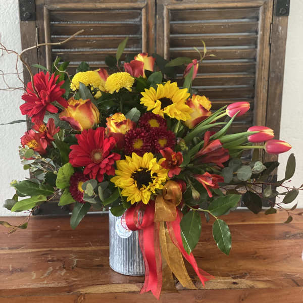 Mixed bouquet of red, yellow, and orange flowers in a metal vase