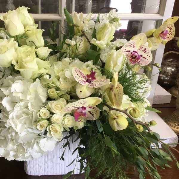 Large white floral arrangement with roses, orchids, and hydrangeas in a white container
