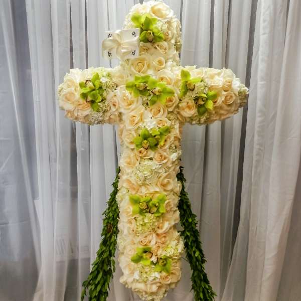 Cross-shaped floral arrangement of cream roses and green orchids with trailing greenery