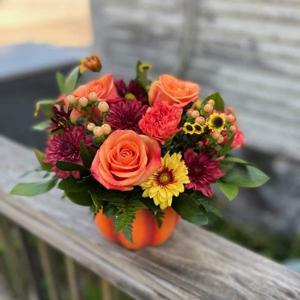 Orange and burgundy flower arrangement in a pumpkin container