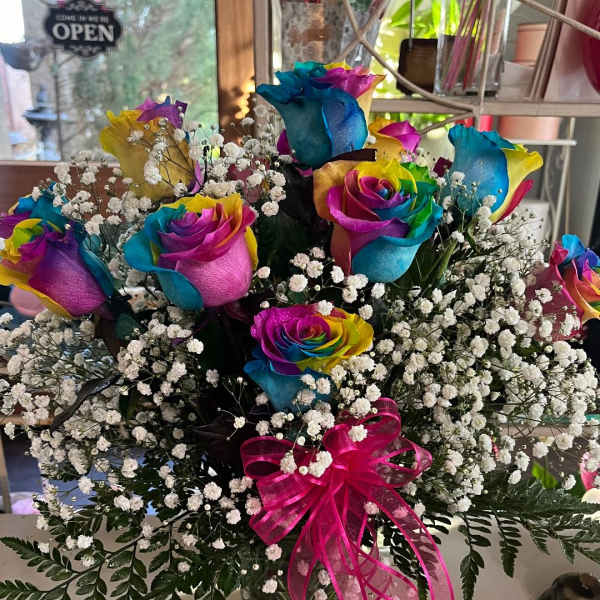 Rainbow-colored roses in a glass vase with baby's breath and a pink ribbon